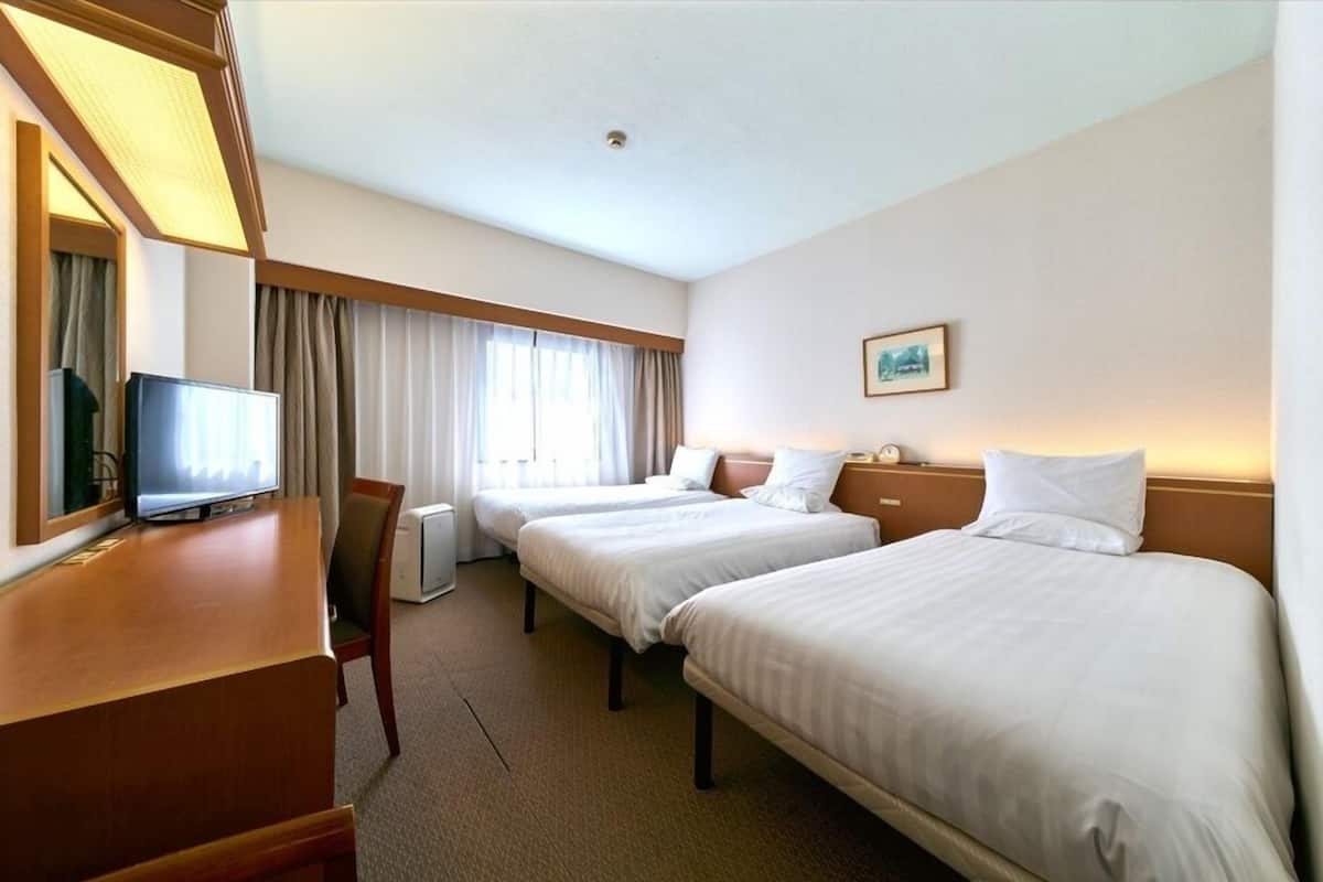 A hotel room with two beds, a desk with a television, and a large window with curtains.