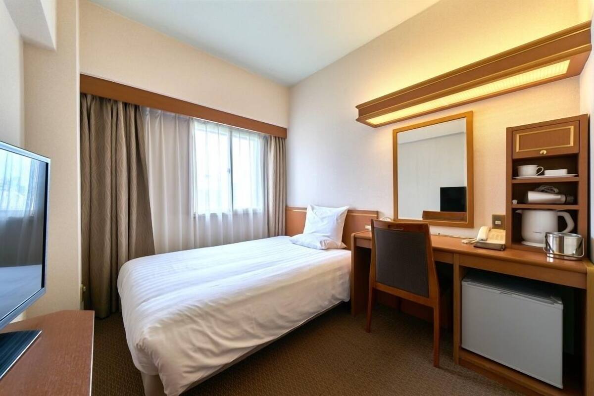 A hotel room with a bed, desk, chair, and a television.