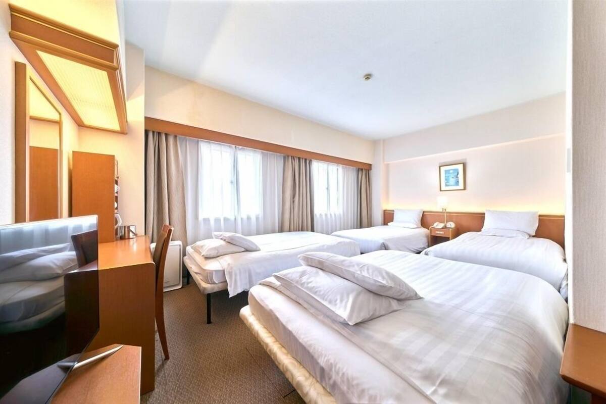 A hotel room with two beds, a desk, a chair, and a window with curtains.