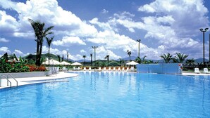 Une piscine entourée de palmiers et de montagnes, avec des chaises longues et des parasols.