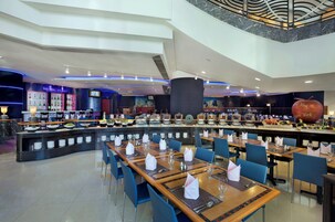 Restaurante moderno com balcão central, diversas mesas de jantar e pé-direito alto com design arquitetônico singular.