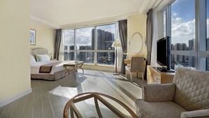 A hotel room with a bed, a sofa, a desk with a TV, a large window with a city view, and a floor lamp. - Harbour Plaza Resort City (Yuen Long)
