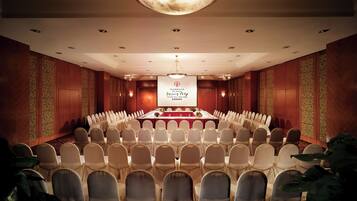 Un salón de conferencias con una mesa larga, filas de sillas y una pantalla de proyector.