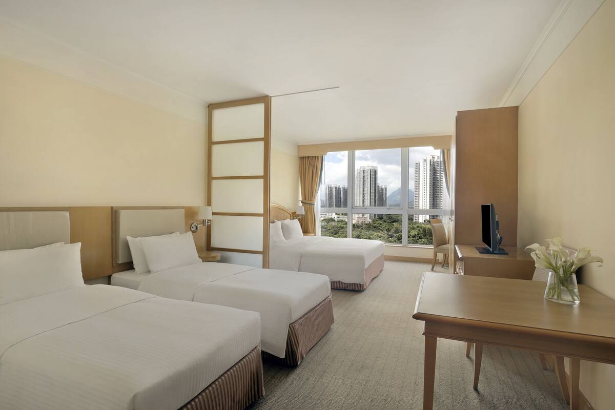 Ein Hotelzimmer mit zwei Betten, einem Schreibtisch, einem Fernseher und Blick auf hohe Gebäude.