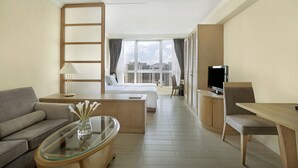 A hotel room with a sofa, a glass-top table with a vase, a bed, a TV, and a view of the city. - Harbour Plaza Resort City (Yuen Long)