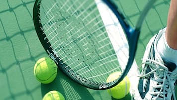 A tennis racket, tennis balls, and a pair of sneakers on a green court.
