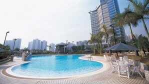 A swimming pool with lounge chairs and umbrellas, surrounded by palm trees and modern buildings in the background. - Harbour Plaza Resort City (Yuen Long)