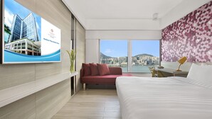 Habitación de hotel moderna con una cama grande, un sofá rojo, un escritorio con una lámpara y un ventanal con vistas a la ciudad.