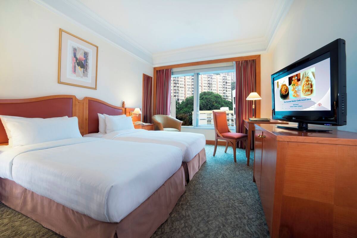 Een hotelkamer met twee bedden, een bureau, een televisie en een raam met uitzicht op de stad.