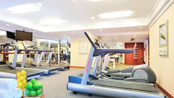Un gimnasio con cintas de correr, pesas y una pared con un cuadro de ejercicios.