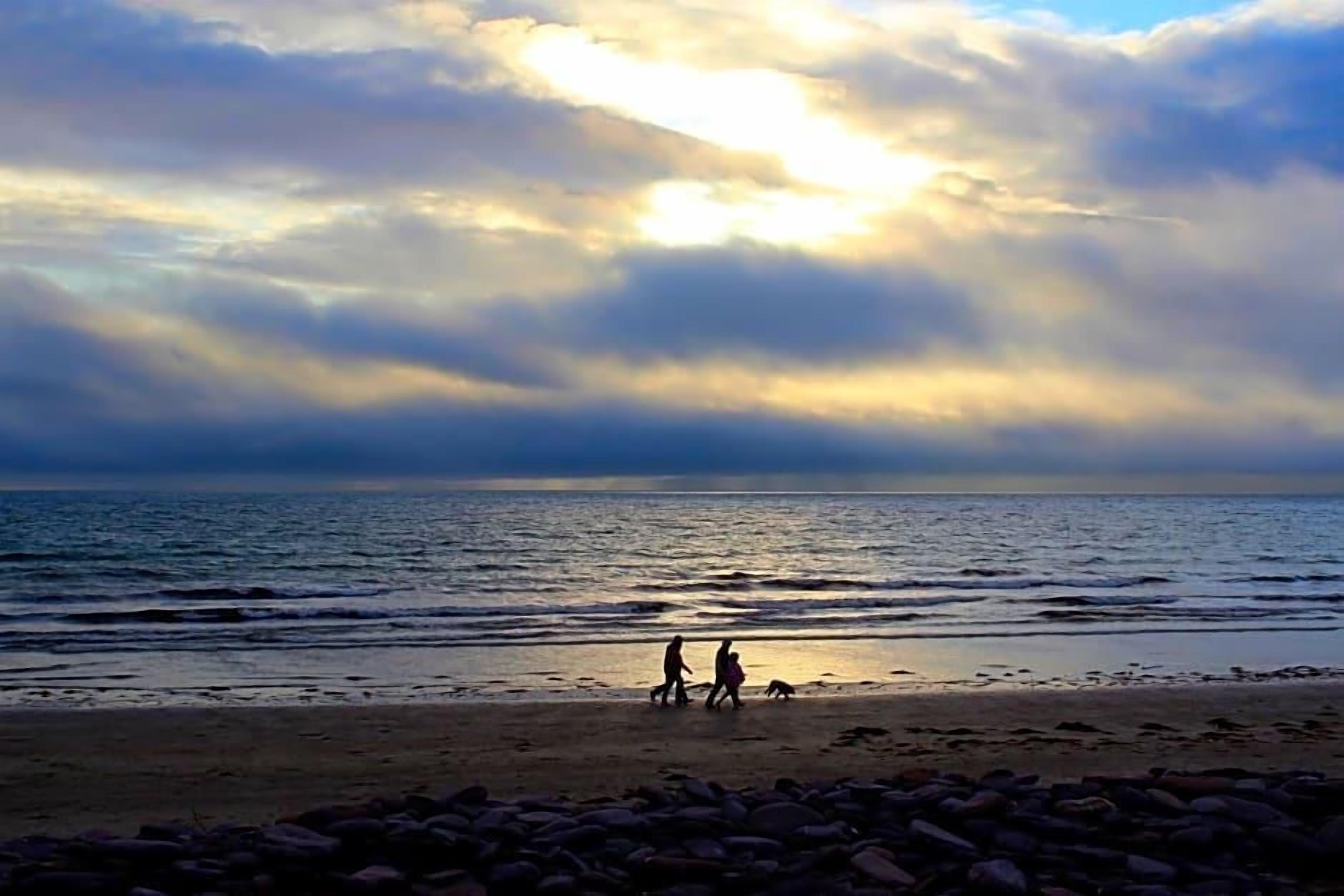 A beach scene with a rocky foreground and a calm sea under a cloudy sky.