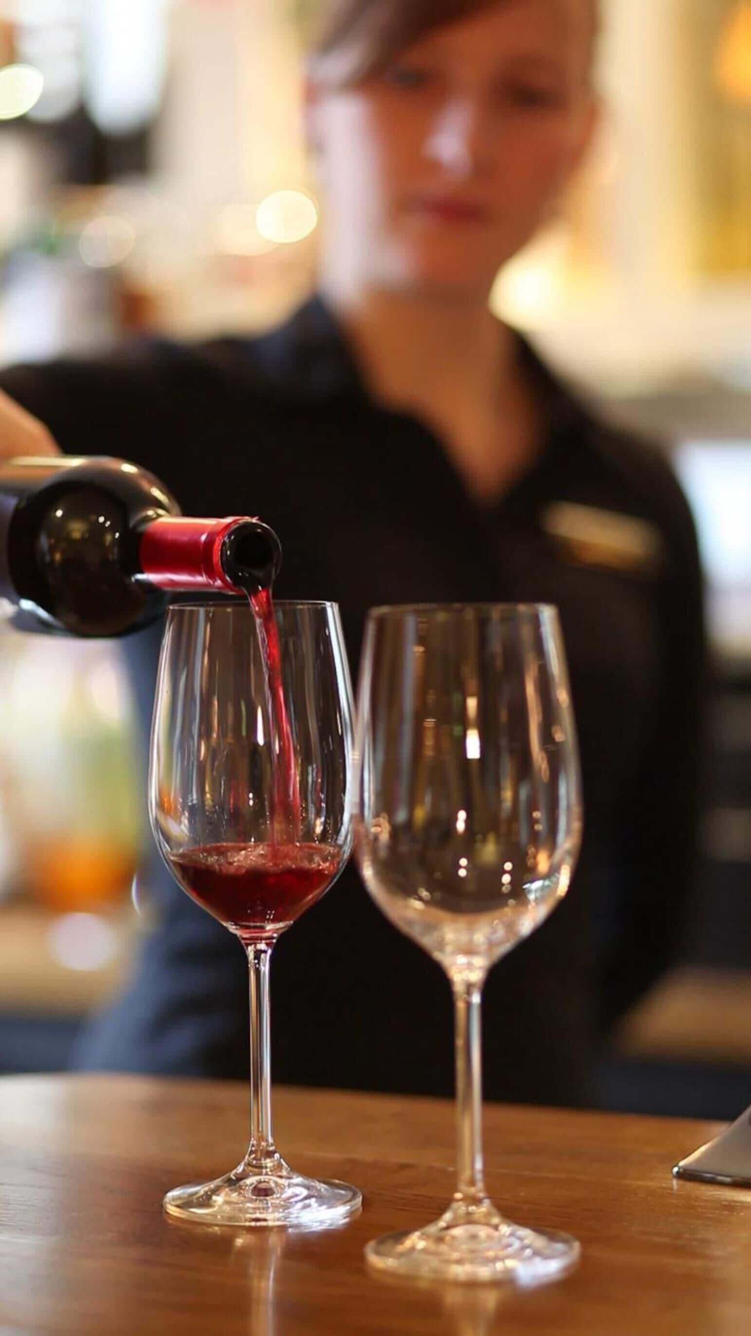 A person pouring red liquid into a wine glass.