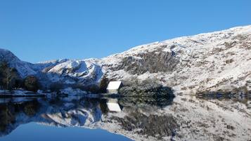 Paisaje montañoso cubierto de nieve con un lago que se refleja y un edificio pequeño.
