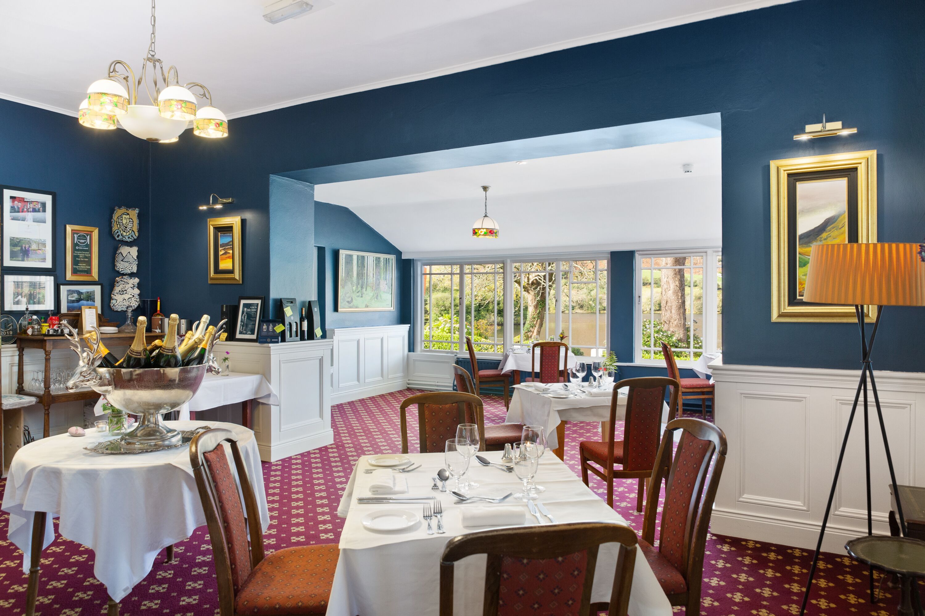 A dining area with tables set for a meal, a chandelier, and framed pictures on the walls.