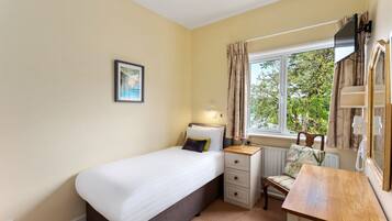 A bedroom with a single bed, bedside table, chair, and a window with curtains.