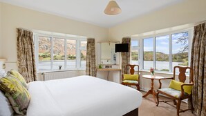 Une chambre d’hôtel avec un grand lit, deux fauteuils, une petite table, un téléviseur et une vue sur un lac.