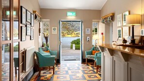 Un hall d’hôtel avec un comptoir d’enregistrement, deux fauteuils turquoise, un sol à motifs, des certificats encadrés et un panneau indiquant la sortie.