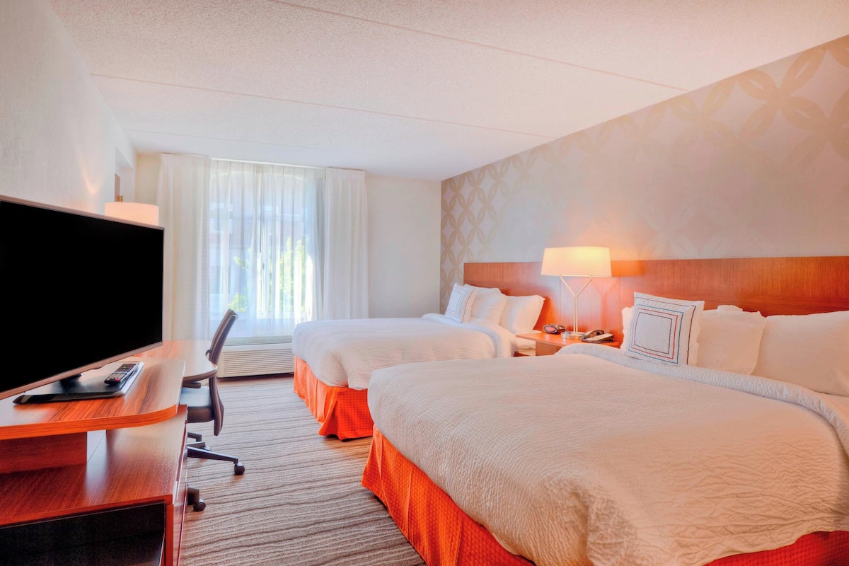 Habitación de hotel con dos camas, un escritorio con televisor y una ventana con cortinas.