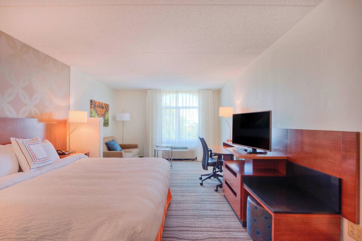 Habitación de hotel con una cama grande, un escritorio, un televisor de pantalla plana, una silla y una mesita.