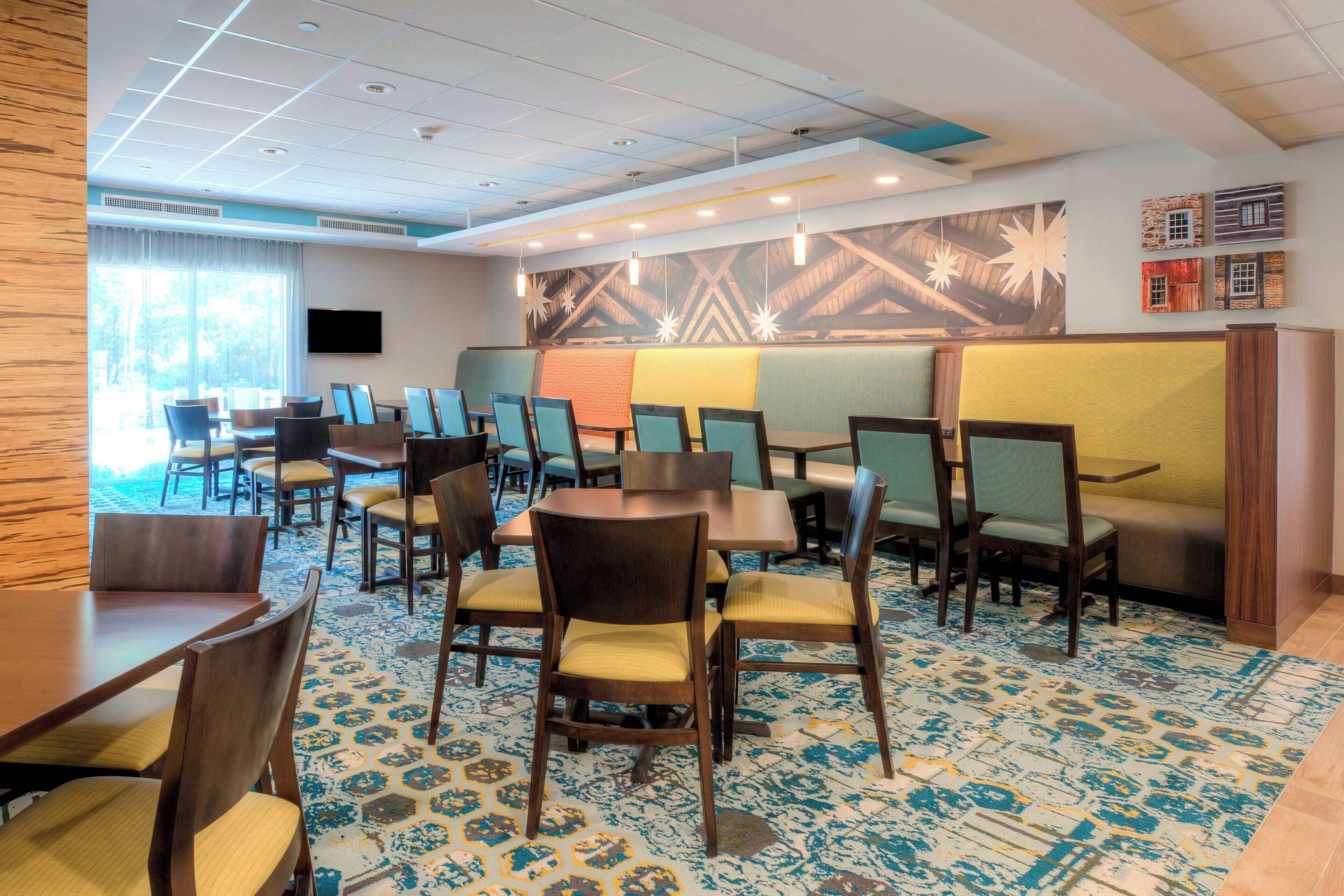 Un comedor de hotel con varias mesas y sillas, una alfombra estampada y un mural grande en la pared.