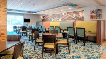 Un comedor de hotel con varias mesas y sillas, una alfombra estampada y un mural grande en la pared.