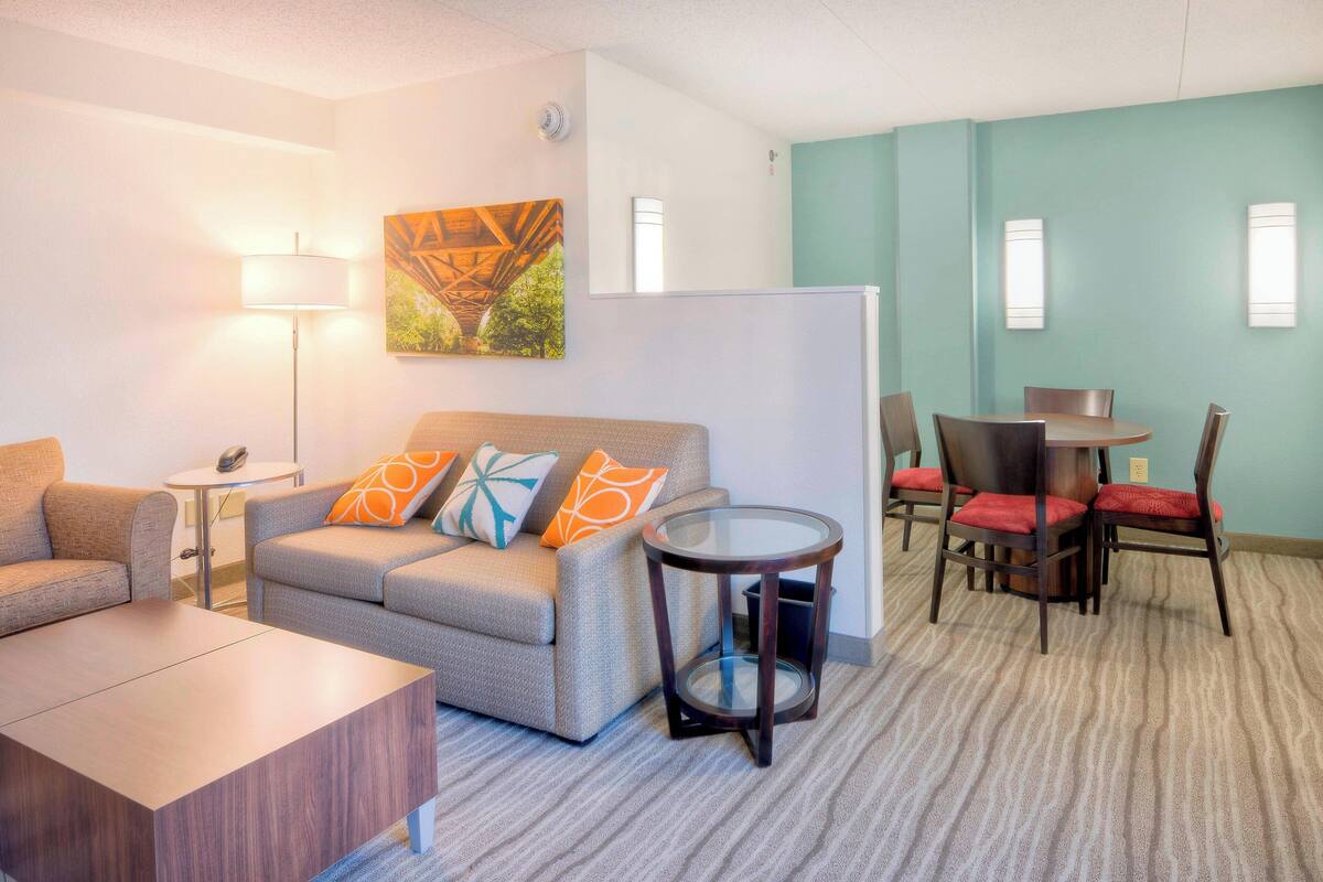Una habitación de hotel con sofá, una pequeña mesa redonda y un comedor con sillas.