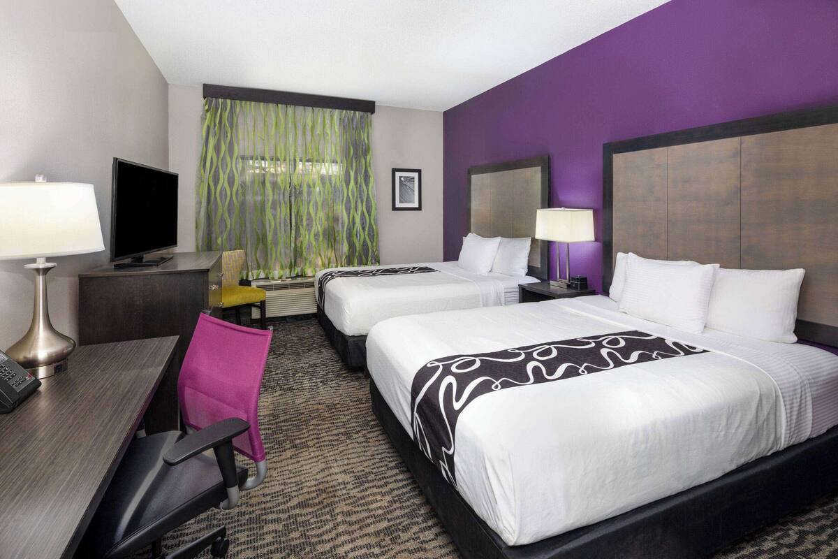 Une chambre d’hôtel avec deux lits, un bureau avec un ordinateur, une chaise et un téléviseur.