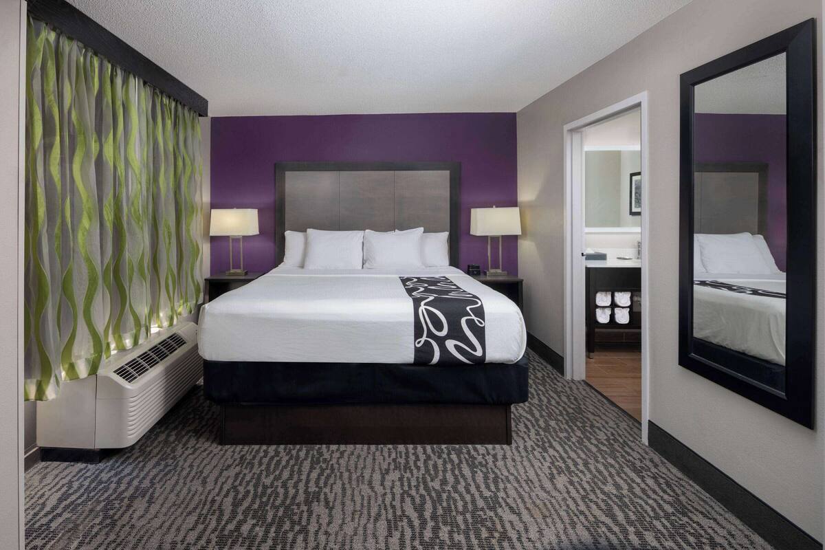 Une chambre d’hôtel avec un grand lit, deux tables de chevet avec des lampes, un miroir et un dressing.