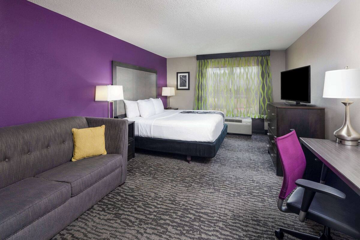 Une chambre d’hôtel équipée d’un lit, d’un canapé, d’un bureau, d’une chaise, d’une télévision et d’une fenêtre avec des rideaux.