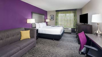 Une chambre d’hôtel équipée d’un lit, d’un canapé, d’un bureau, d’une chaise, d’une télévision et d’une fenêtre avec des rideaux.