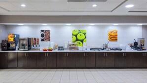 A clean, well-lit breakfast area with a counter displaying various food items and a coffee machine.