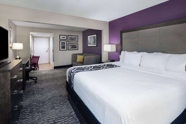 A hotel room with a large bed, a desk with a chair, a television, and a desk lamp.