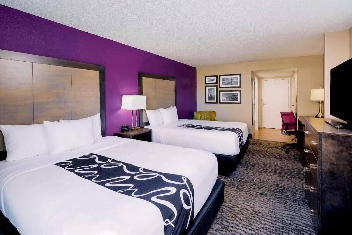 Une chambre d’hôtel avec deux lits, un bureau, une télévision et une porte donnant sur une autre pièce.