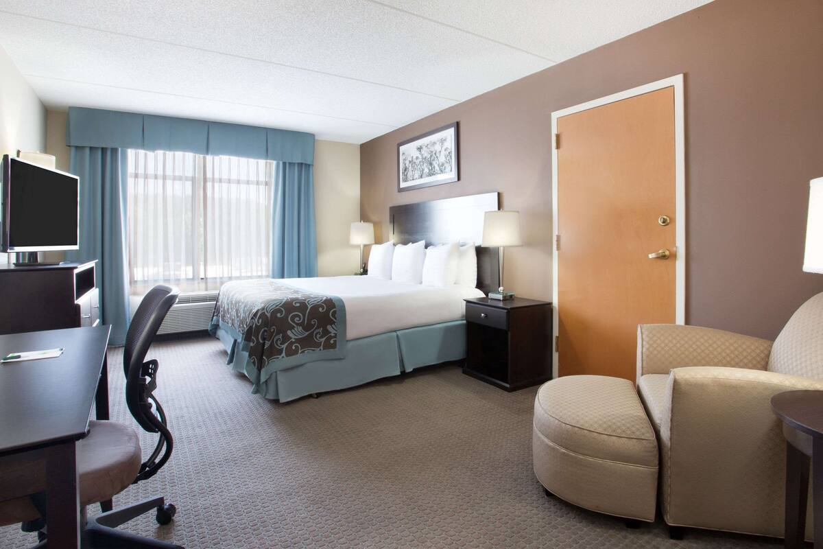 Une chambre d’hôtel avec un lit, un bureau, une chaise et une porte.