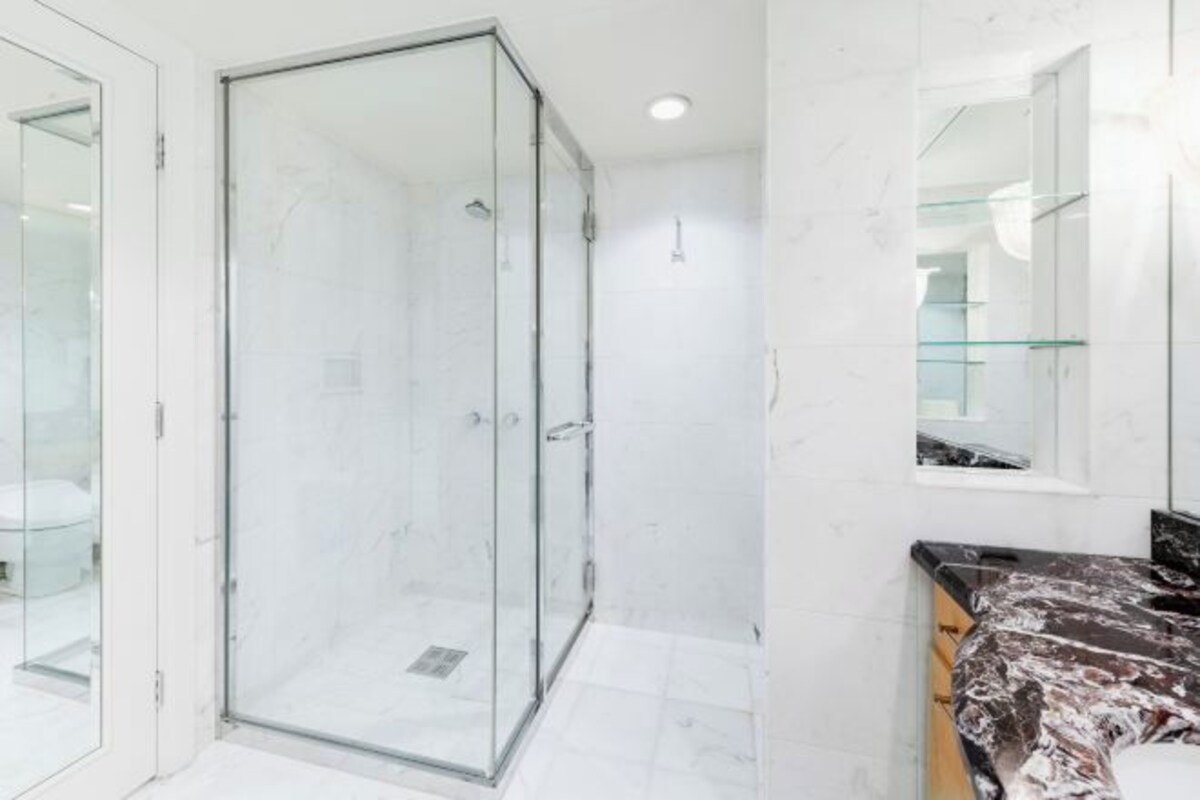 A modern bathroom with a glass shower enclosure, a marble-tiled floor, and a black countertop with a marble pattern.