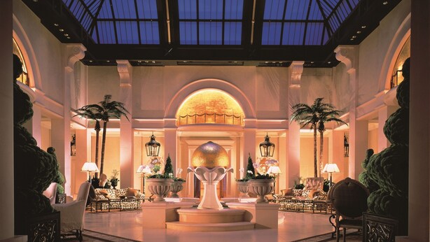A spacious lobby with a high ceiling and a skylight, featuring a central fountain, elegant seating, and palm trees. - Hotel Hankyu International (Osaka)
