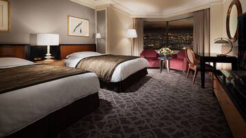 A hotel room with two beds, a desk, a chair, and a view of the city at night.