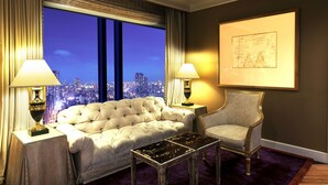 A luxurious bedroom with a large bed, a chair, a table, and a city view through large windows. - Hotel Hankyu International (Osaka)