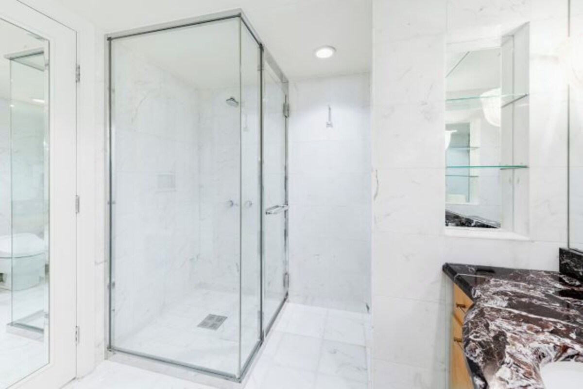 A modern bathroom with a glass shower enclosure, a marble-tiled floor, and a black countertop with a marble pattern.