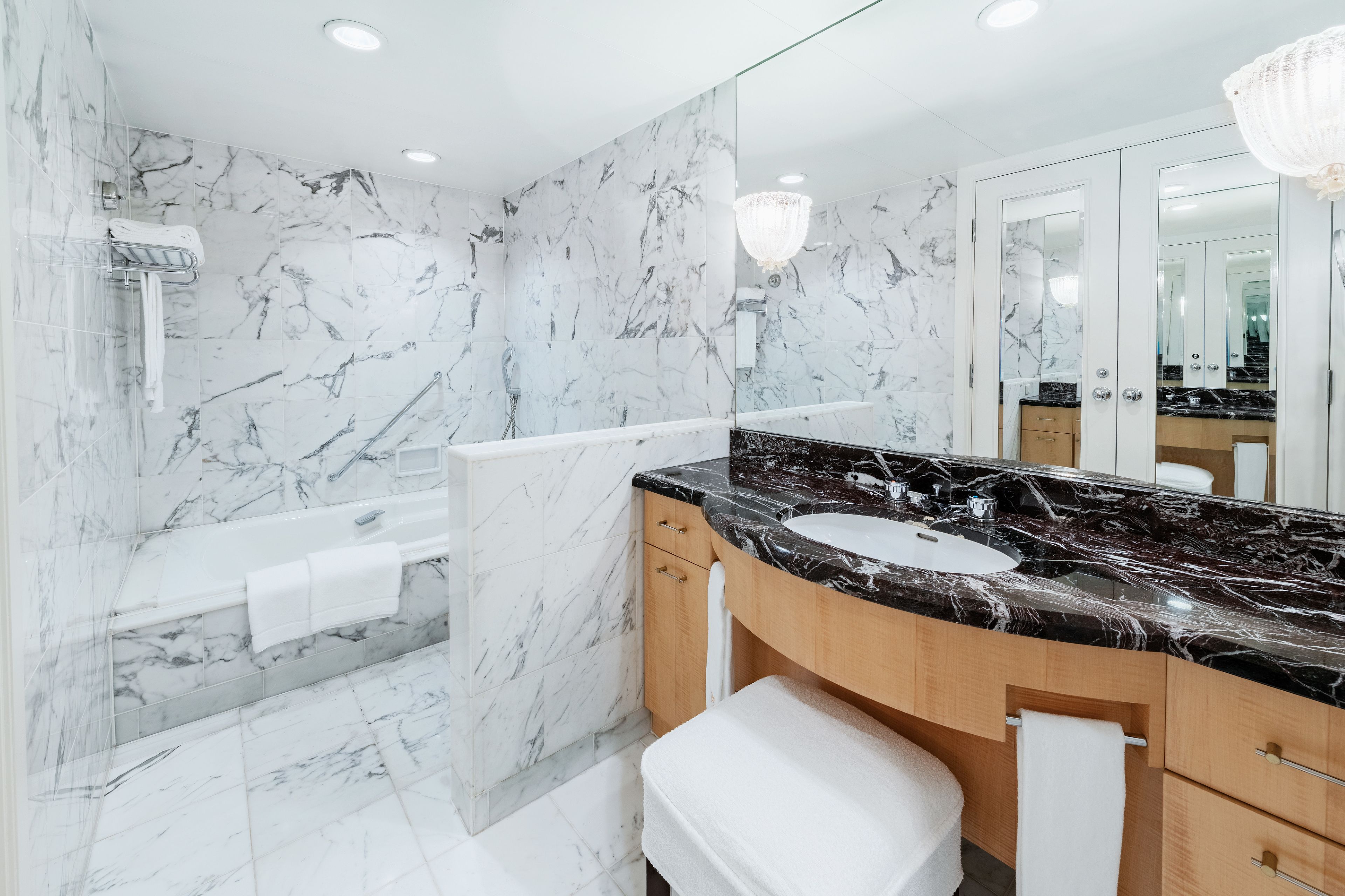 A modern bathroom with a marble wall, a black marble sink, and a glass-enclosed shower.