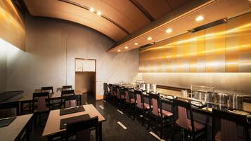 A modern hotel dining area with long tables, chairs, and a buffet setup.