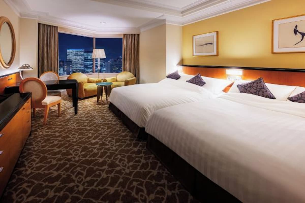 Habitación de hotel con una cama grande, un escritorio, una silla y vistas a la ciudad de noche.