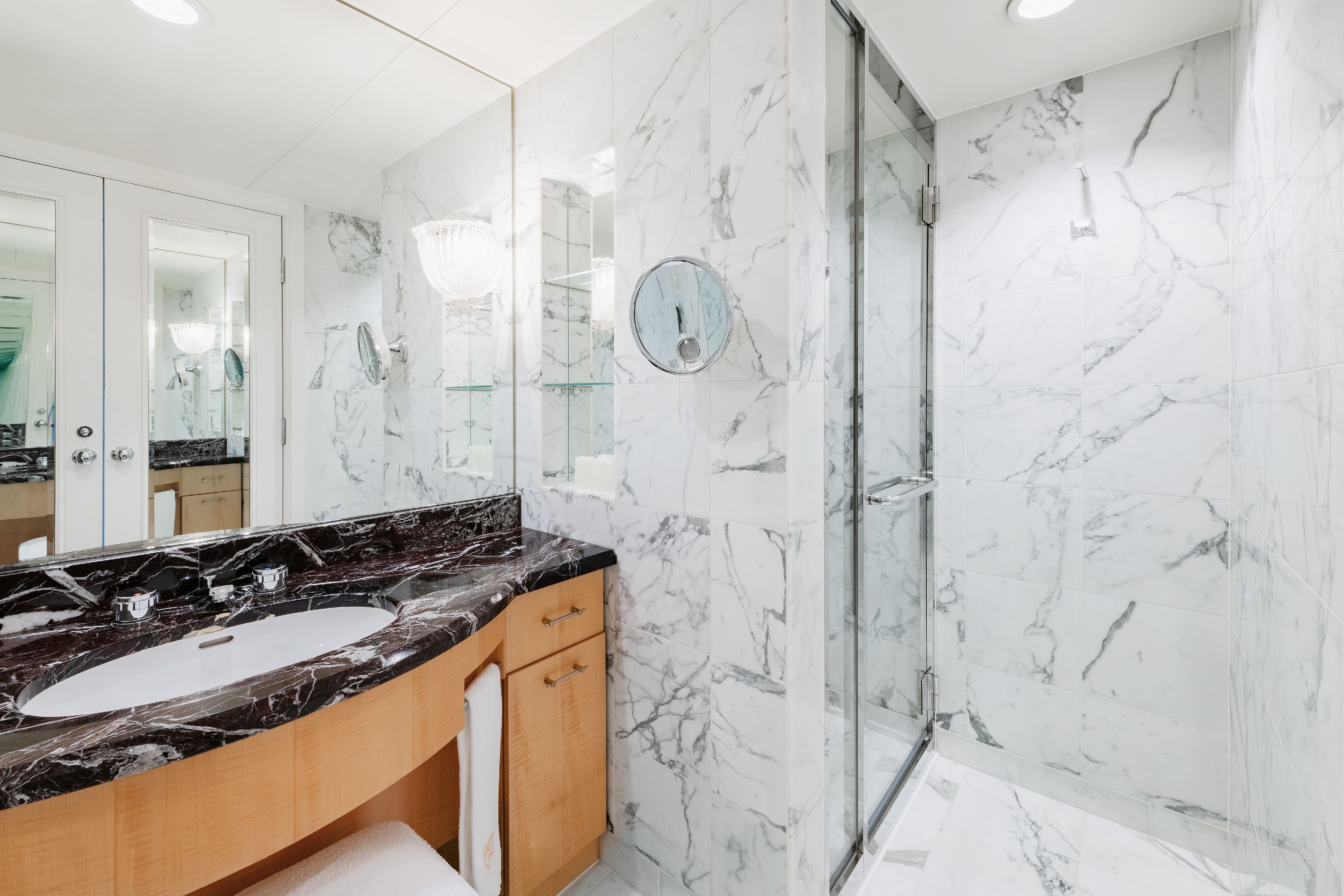 A modern bathroom with a marble vanity, a glass shower enclosure, and a large mirror.