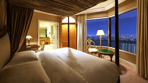 A hotel room with a large bed, a view of the city at night, a sitting area with a table and chairs, and a bathroom visible through an open door. - Hotel Hankyu International (Osaka)
