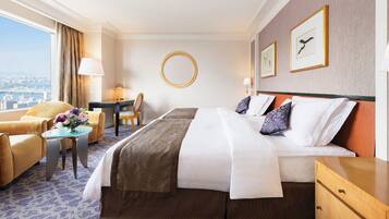 A hotel room with a large bed, a desk, a chair, and a view of the city.