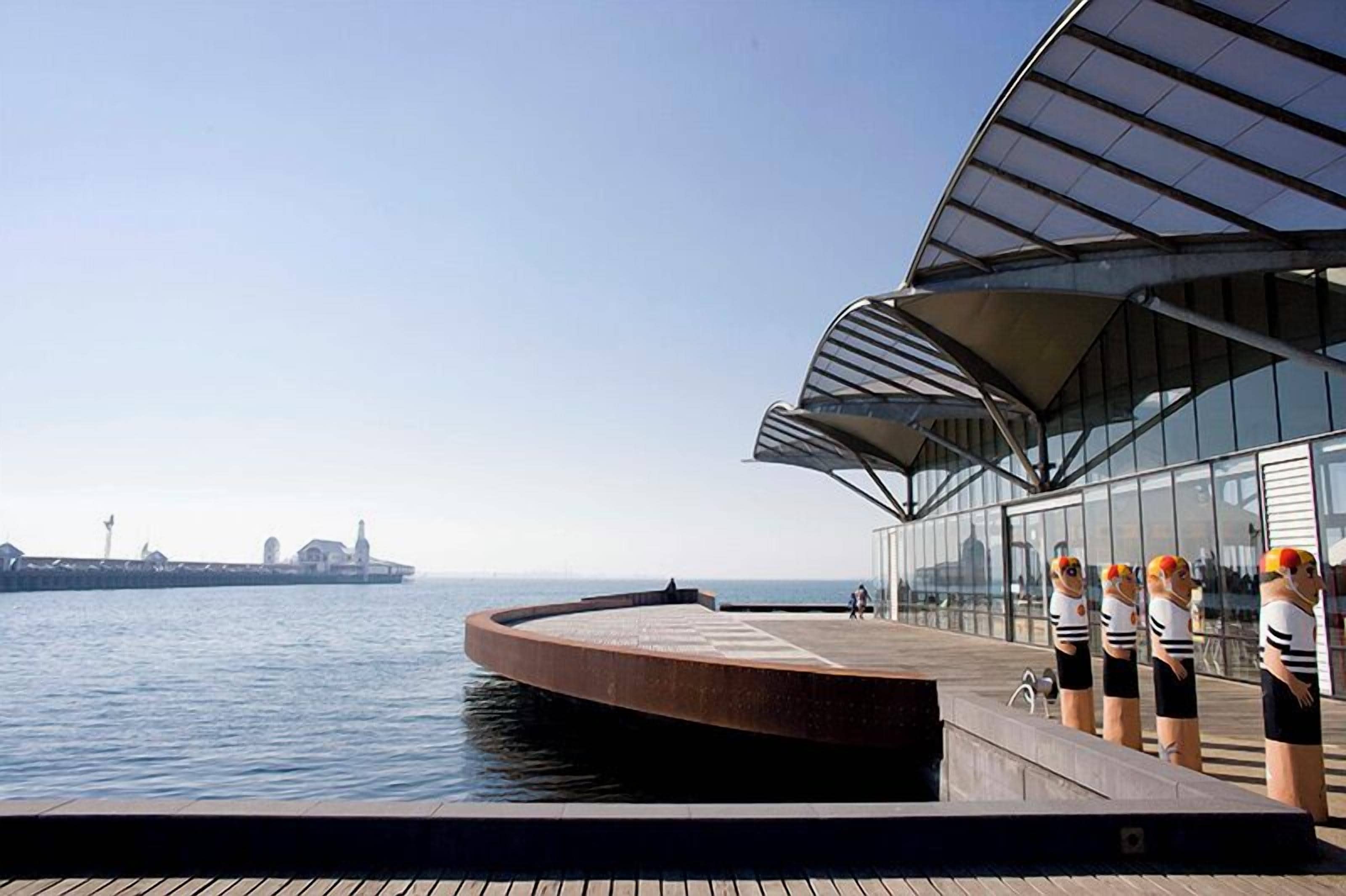 A waterfront building with a curved roof and a glass facade overlooking the water.