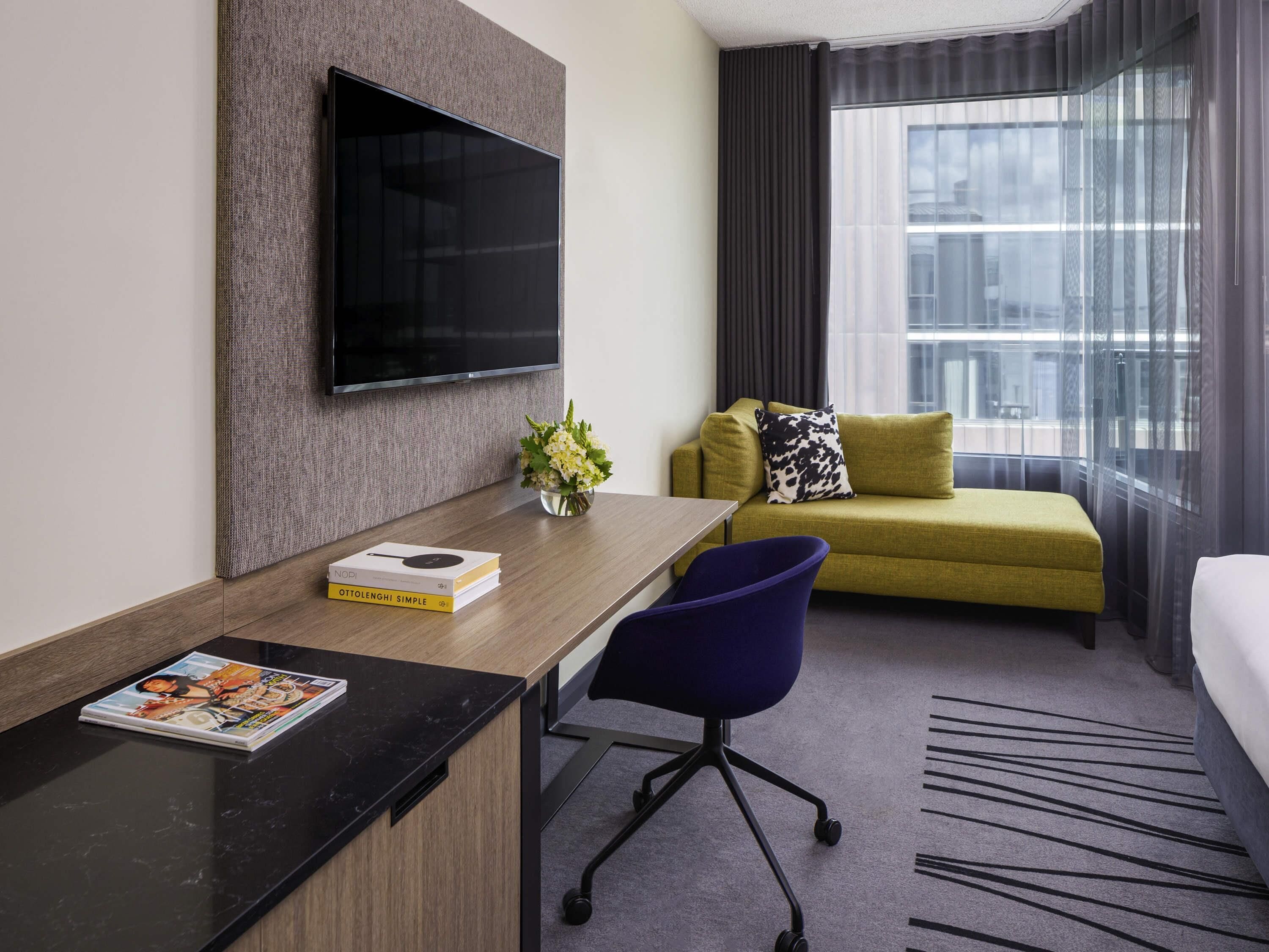 A hotel room with a desk, a sofa, a TV, and a window with curtains.