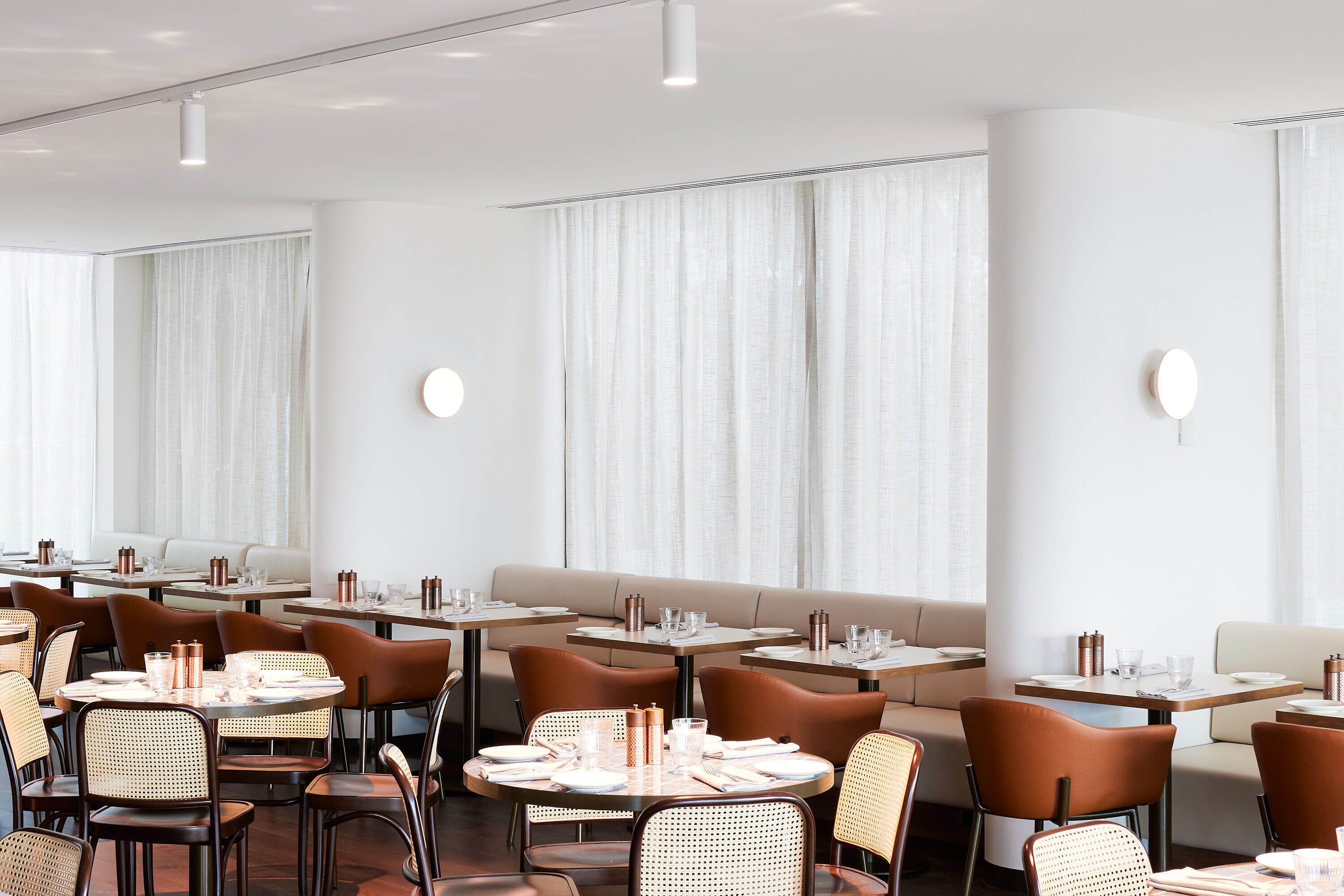 Un espace repas moderne avec des tables rondes, des chaises marron et un coin salon central agrémenté d’un canapé.