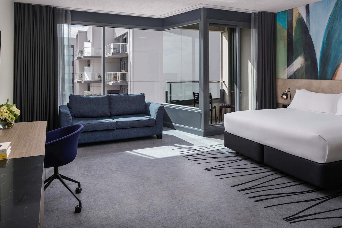 Una habitación de hotel moderna con cama, sofá, escritorio y un ventanal grande.