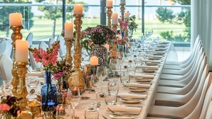 Una larga mesa de comedor dispuesta con velas, copas y arreglos florales, con vistas a un paisaje exuberante.
